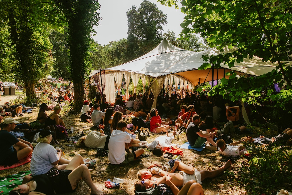 many people seated and lying on grass while spiritual activities go on under some sort of gazebo